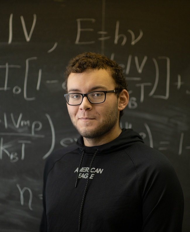 physics student pictured in front of a chalkboard.