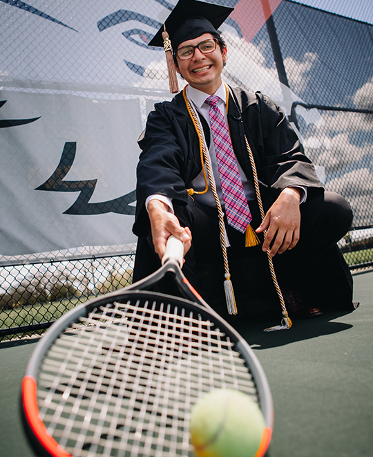 Photo of Matt in his cap an gown with a tennis racket and ball