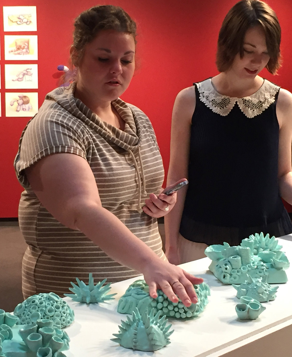 student touching a ceramics display at a gallery opening. 