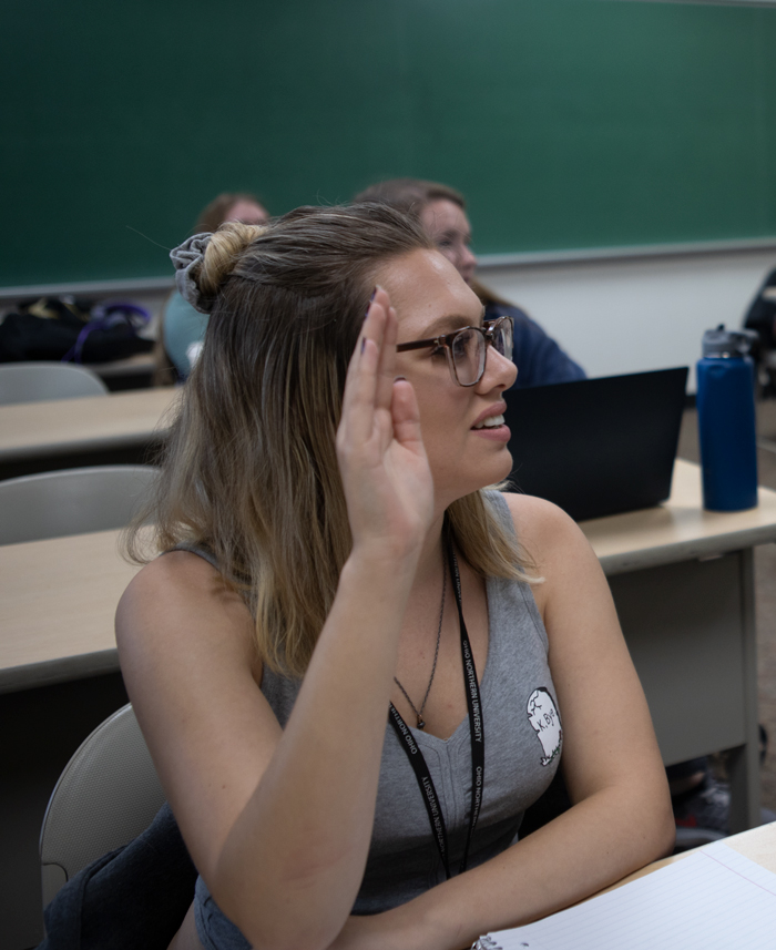 psychology student raising her hand to participate in a classroom lecture.