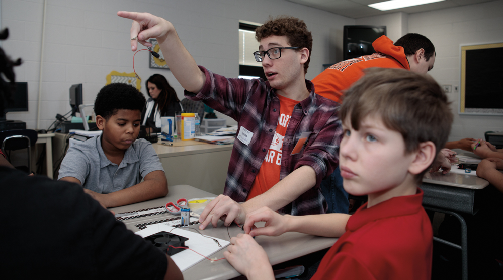 engineering education student works with kids on an experiment. 