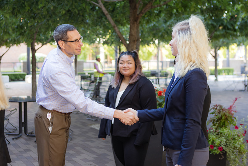 Students dressed in business attire shaking hands with executives