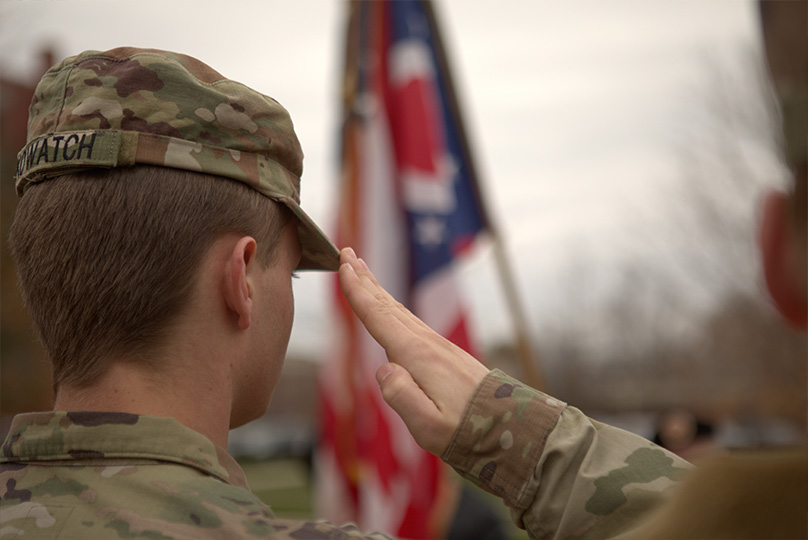 Photo of Military person saluting with flag in the background
