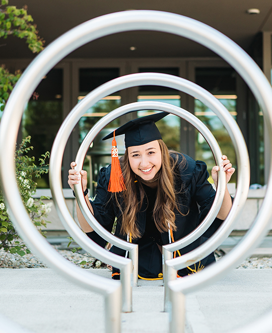 Photo of Olivia in her cap and gown looking through bike rack