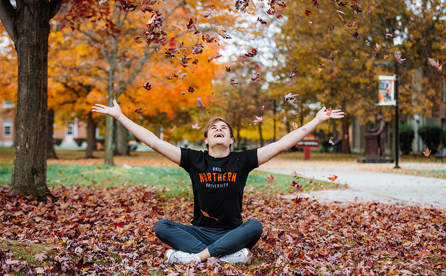 ONU student throwing fall leaves up