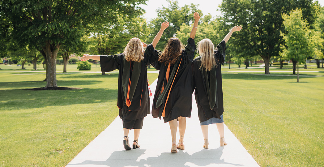 photo of 3 pharmacy students with their caps and gowns on walking on campus