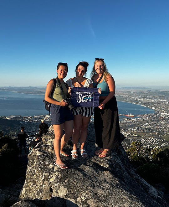 Photo of Mallory with 2 other individuals at a top of a high rock