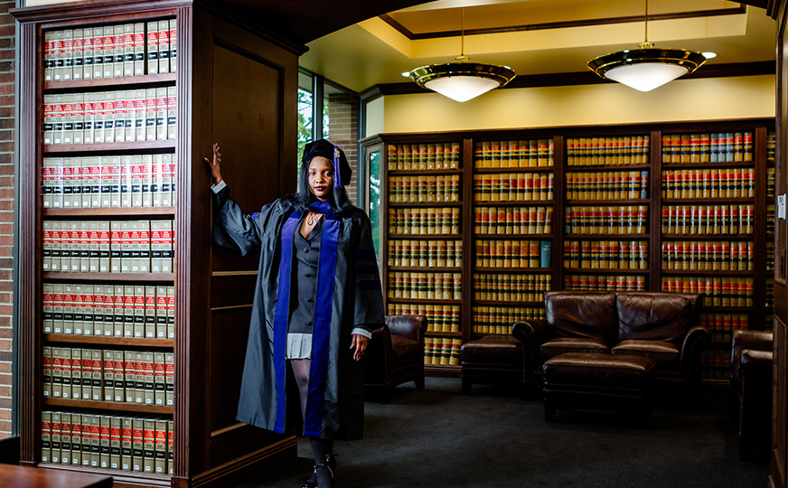 Photo of Camila in her graduation garb posing in the law library