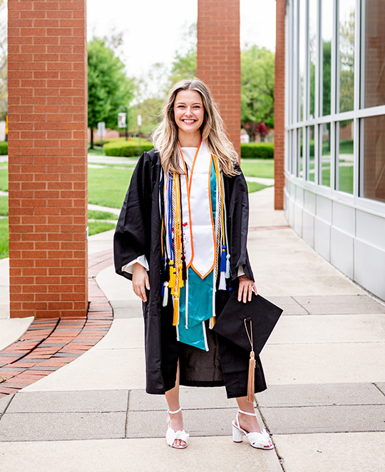 Photo of Chrissy in her graduation cap and gown posing outside