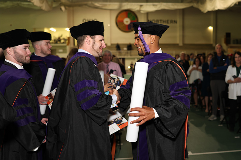Photo of 2 ONU graduates shaking hands and smiling 
