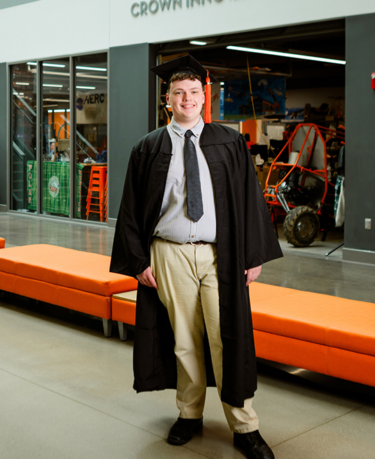 Photo of Kaden in his graduation gown posing inside 