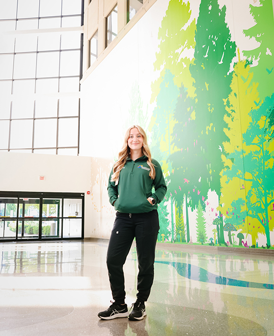 Photo of Ashley posing in front of wall art of trees