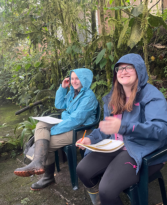 Photo of 2 ONU student in rain jackets with their hood up sitting in chairs