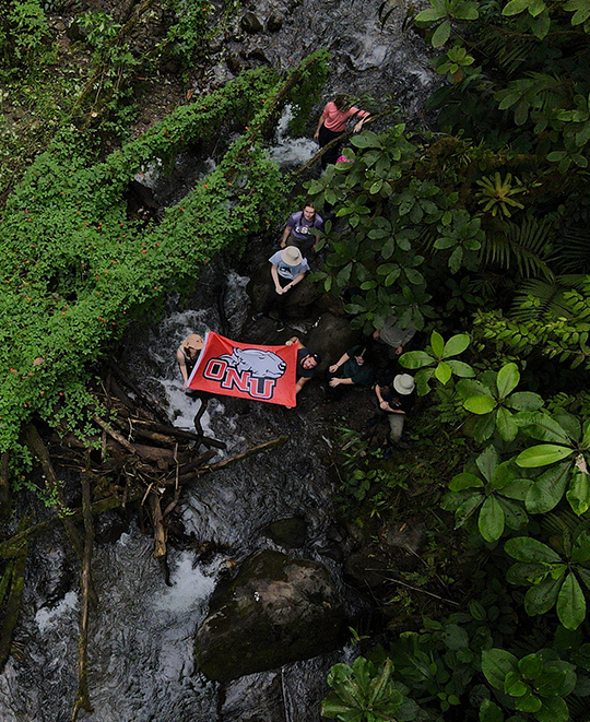 Ariel shot of student group walking in the forest holding ONU flag out