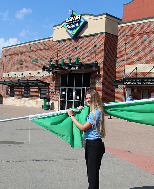 Photo of Chloe holding a green flag outside of Dayair Credit Union Ballpark