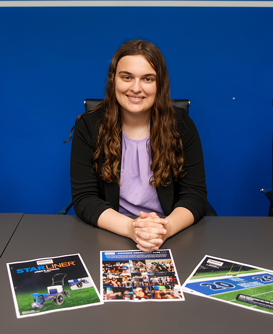 Ella sitting behind a desk with 3 of printouts of design work