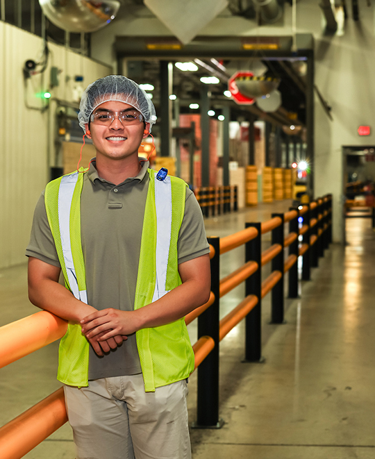 Photo of Long posing in a corridor wearing a hair net and reflective vest