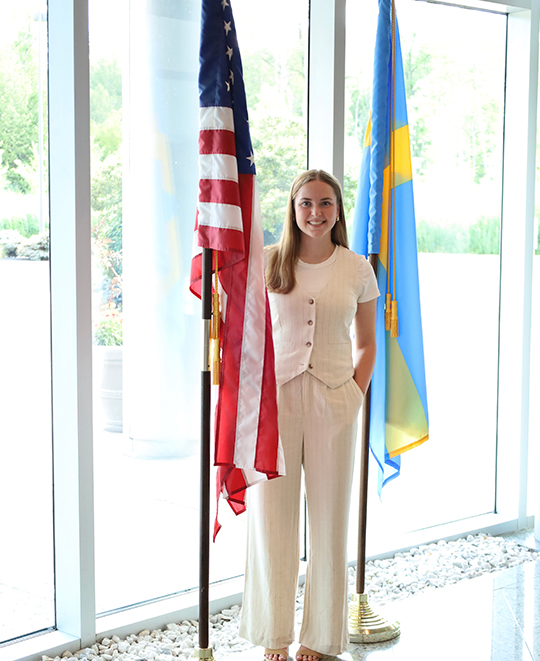 Photo of Rylie posing between 2 flags - one being the United States of America flag