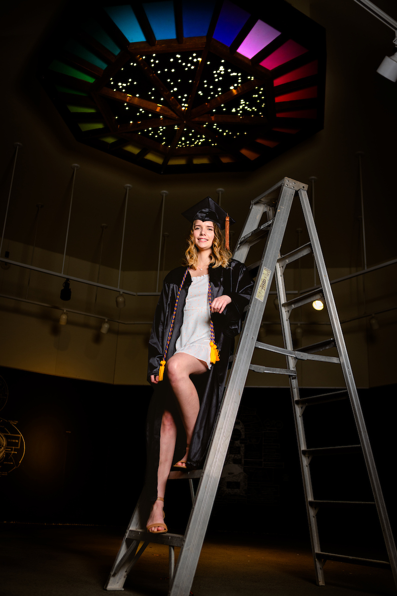 Lily posing in grad robe on ladder in the dance studio