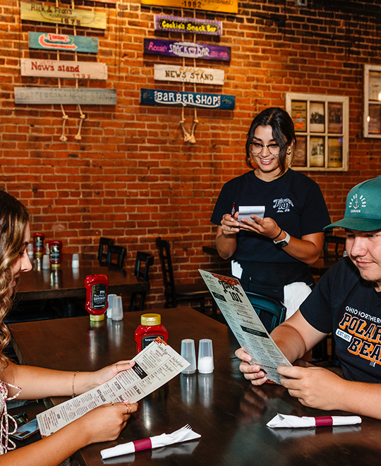 Photo from the Tavern Restaurant, 2 students sitting at a table holding menus with waitress
