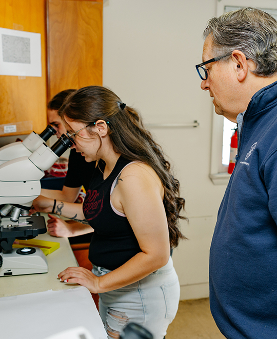 Photo of 2 ONU students looking through microscopes while the instructor is overseeing