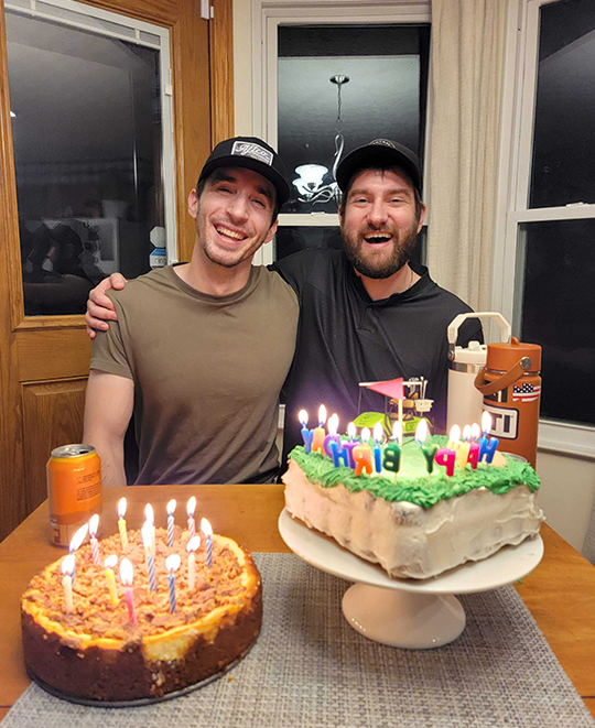 Photo of 2 friends seated in front of cakes with candles lit
