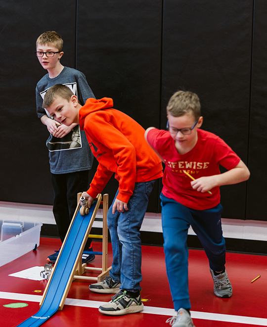 Photo of 3 young boys watching as the wooden car drives on the ramp