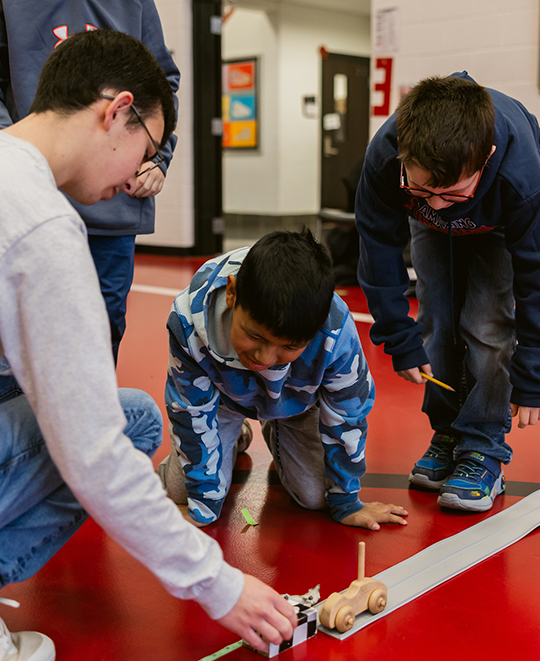 Photo of 2 young students working with an ONU student on the ending ramp