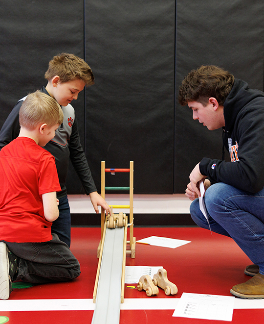 Photo of 2 young boys working with an ONU student on their ramps and cars