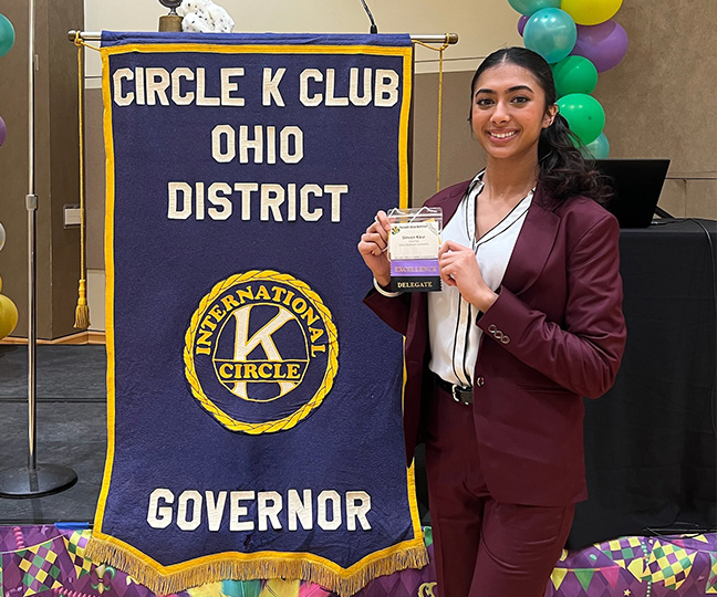 Simran posing next to a circle K club ohio district governor flag on a stage
