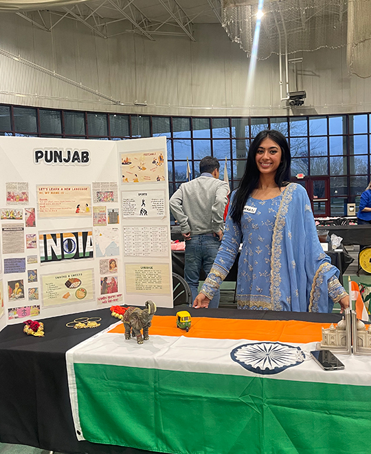 Presentation table with a poster titled Punjab on it and the presenter behind the table in a blue Punjab on.