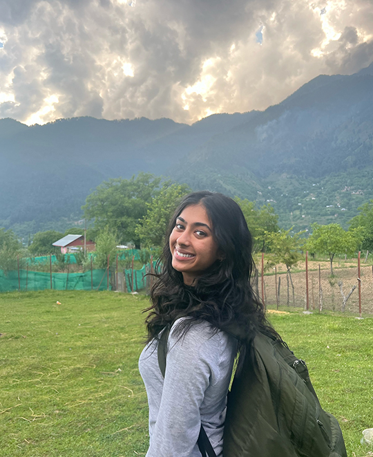 Young lady looking back over her shoulder in an open field with mountains in the background