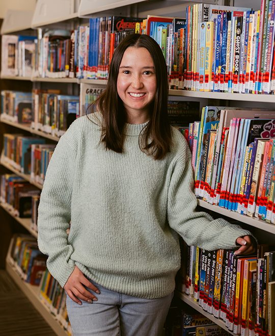 Eva posing beside a library shelves full of books