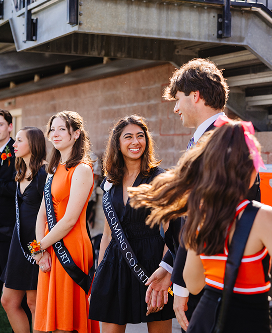Homecoming pairs waiting on the field where the ladies are wearing their sashes