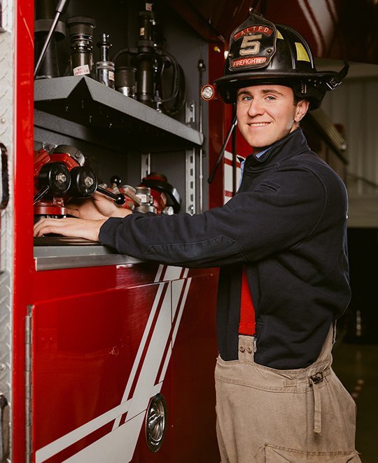 Michael with his fireman hat checking the fire truck gear, posing for camera