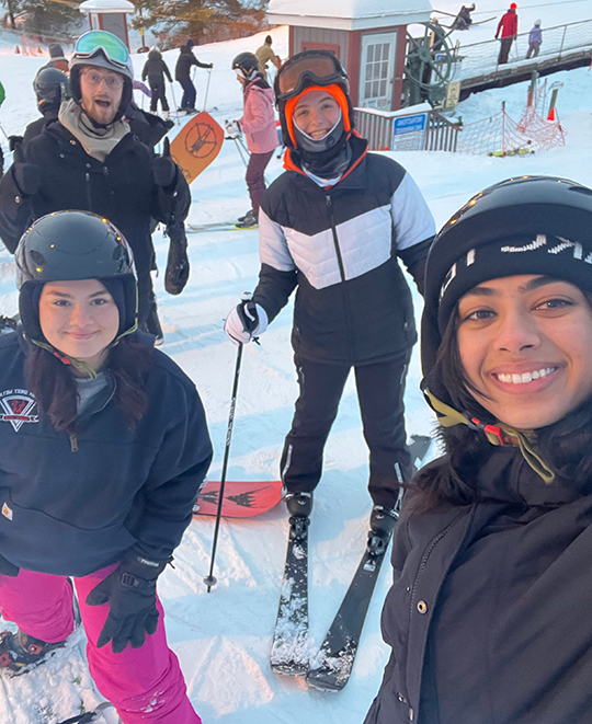 Snow selfie of 4 friends in warm clothing in the snow with skis on posing together
