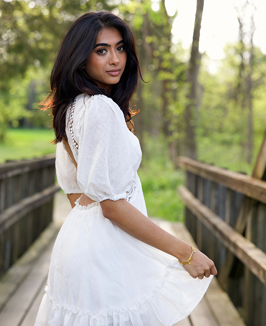 Simran in a white dress on a wooden bridge looking back over her shoulder