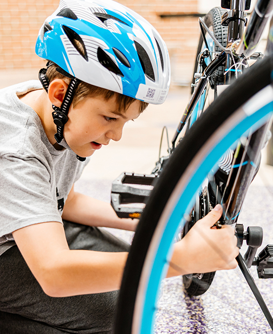 One of the kiddos with a helmet on working on the chain of his bike