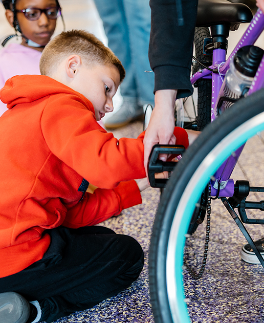 Another child being shown how to put the chain on the bike while another kid is watching