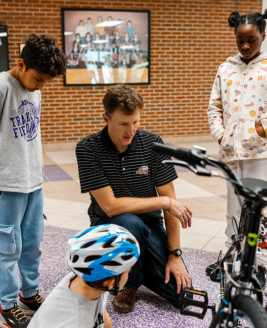 Another adult mentor explaining the function of bicycle parts while several children listen