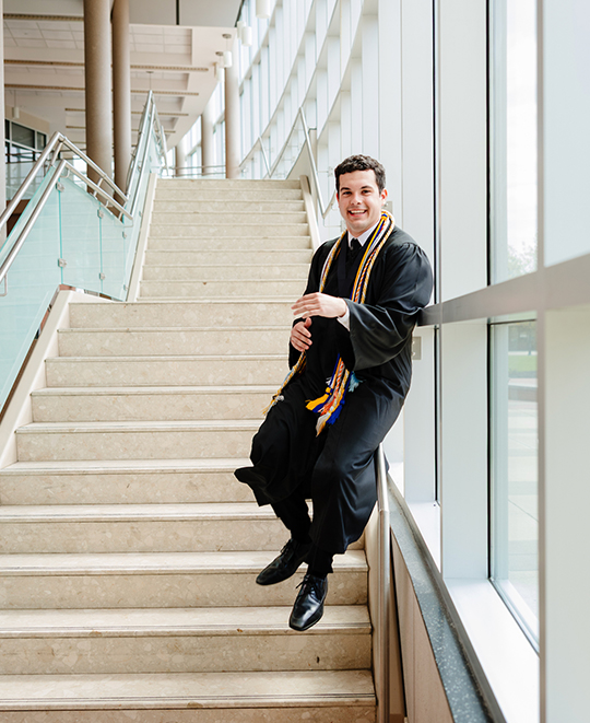 Drew sliding down a staircase rail in his graduation gown