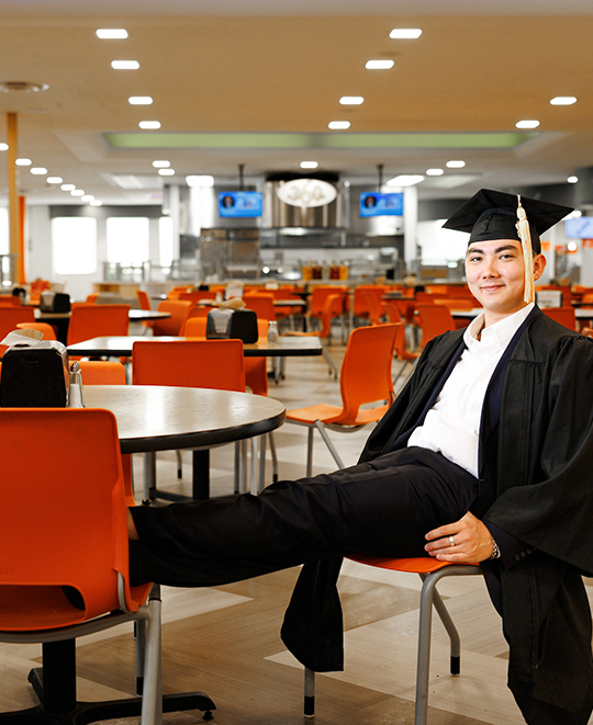 Dylan in Macintosh seated on one chair with his feet up on another chair