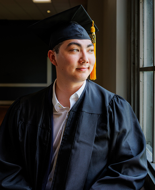 Dylan in his cap and gown looking out a window