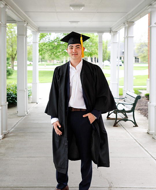 Dylan posing in a white porched area posing in his cap and gown