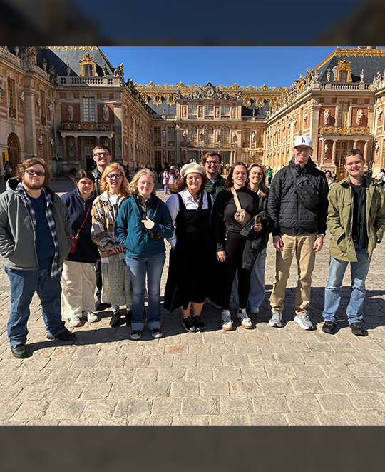 A group of Ohio Northern University students and Professor Russ Crawford posing in the cobblestone courtyard of the Palace of Versailles during their World War II memory tour.