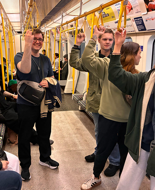 Ohio Northern University students traveling on a European tram, holding onto yellow overhead straps while navigating between historic sites during their World War II memory tour.