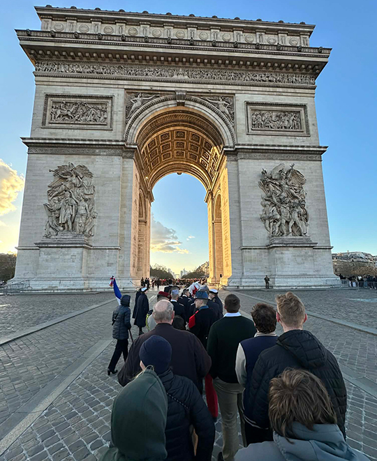 Ohio Northern University students standing at the base of the Arc de Triomphe in Paris, in front of the massive stone relief sculpture "La Marseillaise," which depicts a winged figure leading a group of soldiers.