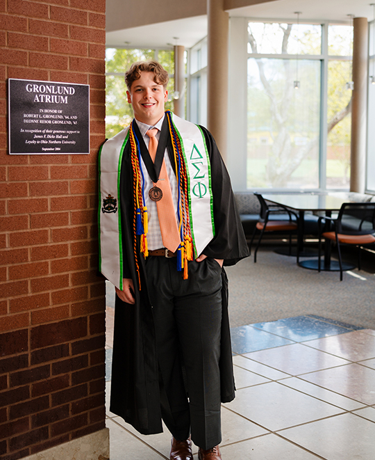 Jordan leaning against the wall next to the Gronlund Atrium sign