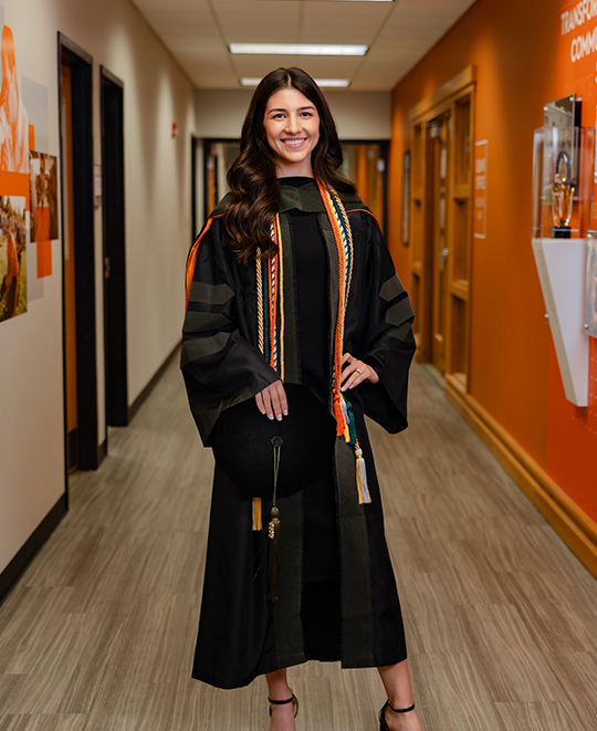 Samantha posing in her graduation gown in the pharmacy building hallway