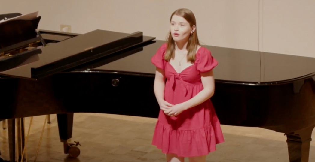 Student singing on stage in front of a piano